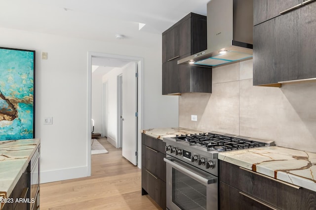 kitchen featuring wall chimney range hood, dark brown cabinets, tasteful backsplash, high end stove, and light hardwood / wood-style floors