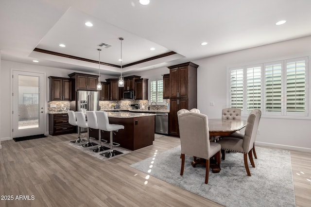 dining room with sink, crown molding, light hardwood / wood-style flooring, and a raised ceiling