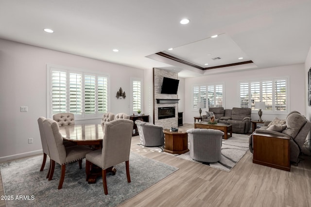 dining room with light hardwood / wood-style floors, crown molding, a raised ceiling, and a fireplace