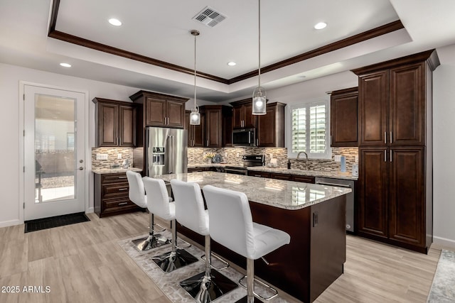 kitchen featuring appliances with stainless steel finishes, light stone countertops, pendant lighting, a kitchen island, and a tray ceiling