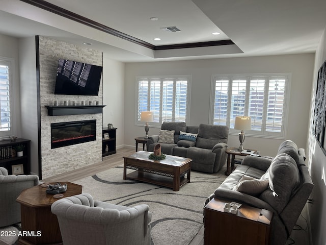 living room featuring a fireplace, a tray ceiling, crown molding, and light hardwood / wood-style flooring