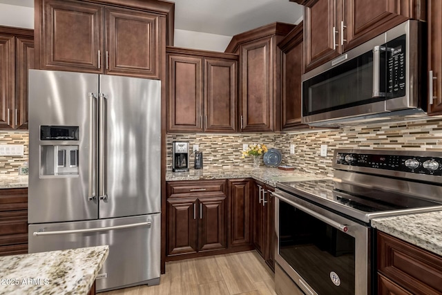 kitchen with stainless steel appliances, dark brown cabinets, decorative backsplash, and light stone countertops