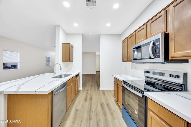 kitchen with light stone countertops, appliances with stainless steel finishes, light hardwood / wood-style floors, and sink