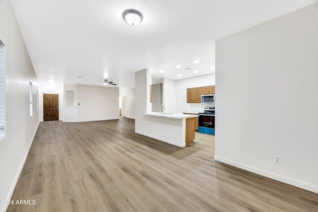 unfurnished living room with ceiling fan, light wood-type flooring, and sink