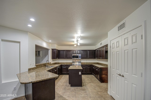 kitchen with dark brown cabinetry, sink, kitchen peninsula, a kitchen island, and stainless steel appliances