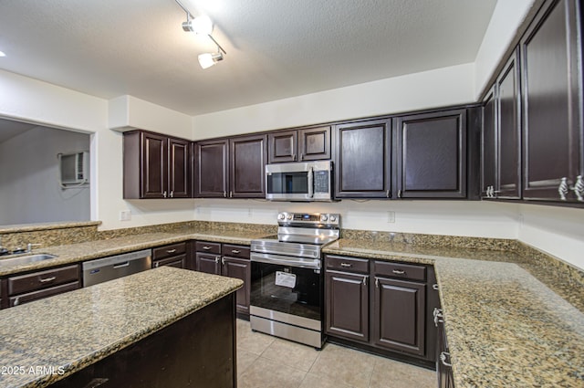 kitchen with appliances with stainless steel finishes, rail lighting, light tile patterned floors, dark brown cabinetry, and a wall unit AC