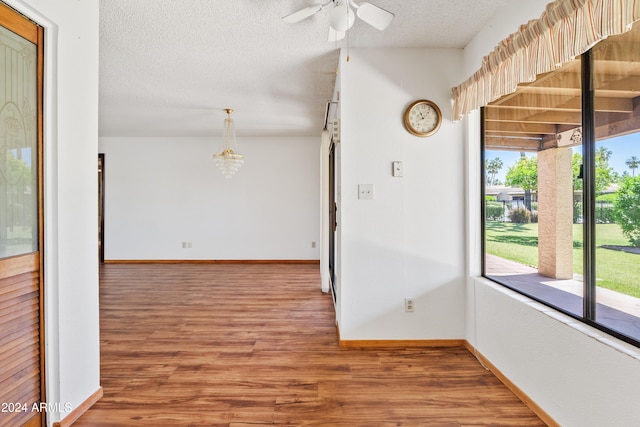 spare room featuring ceiling fan with notable chandelier, a textured ceiling, baseboards, and wood finished floors