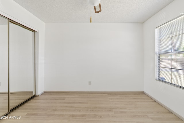 unfurnished bedroom featuring a textured ceiling, a ceiling fan, baseboards, light wood-style floors, and a closet