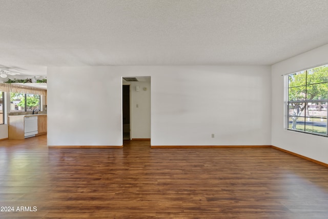 empty room featuring a textured ceiling, a sink, wood finished floors, and baseboards