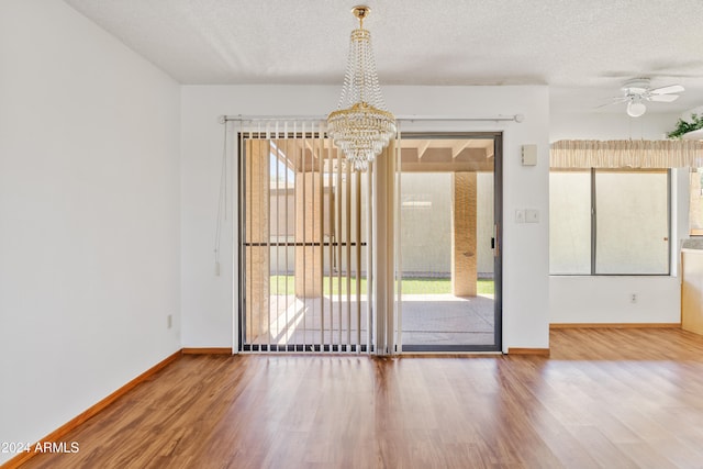 spare room with ceiling fan with notable chandelier, a textured ceiling, baseboards, and wood finished floors