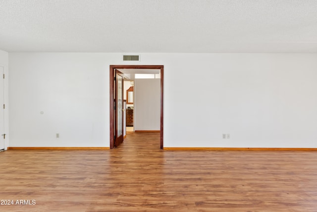 unfurnished room with a textured ceiling, wood finished floors, visible vents, and baseboards