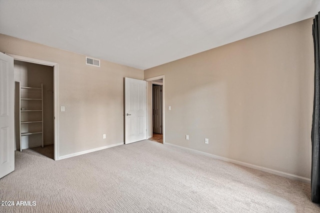 unfurnished bedroom with a walk in closet, a closet, and light colored carpet