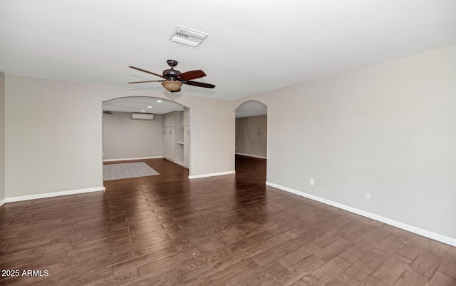 spare room featuring ceiling fan, arched walkways, visible vents, baseboards, and dark wood-style floors