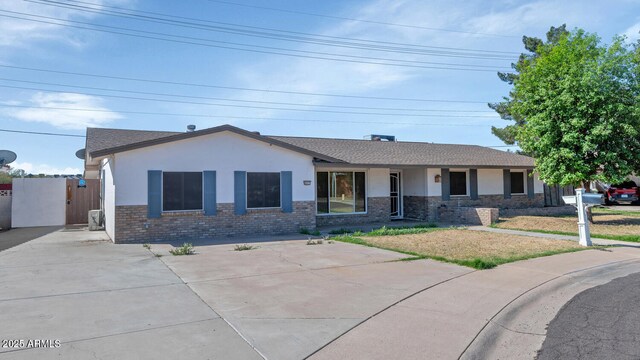 ranch-style house featuring concrete driveway, roof with shingles, stucco siding, a front lawn, and brick siding