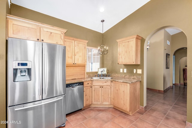 kitchen with light brown cabinetry, stainless steel appliances, hanging light fixtures, and lofted ceiling