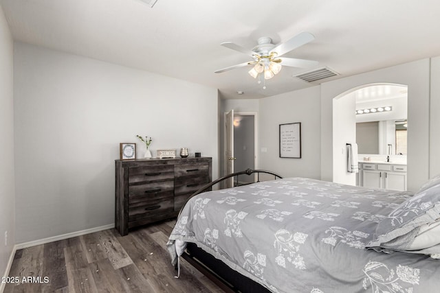 bedroom with visible vents, ensuite bathroom, wood finished floors, arched walkways, and baseboards