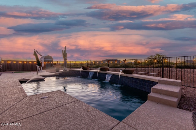 pool at dusk with pool water feature and a patio area