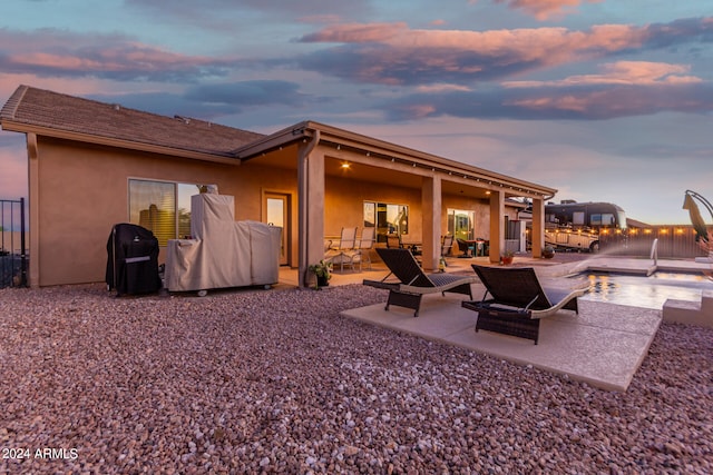 back house at dusk with a fenced in pool and a patio area