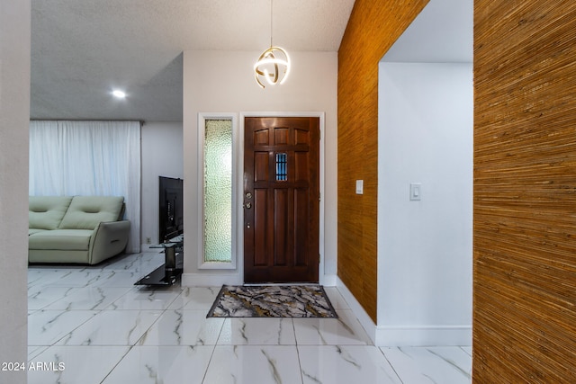 entryway featuring a notable chandelier, a textured ceiling, and wood walls