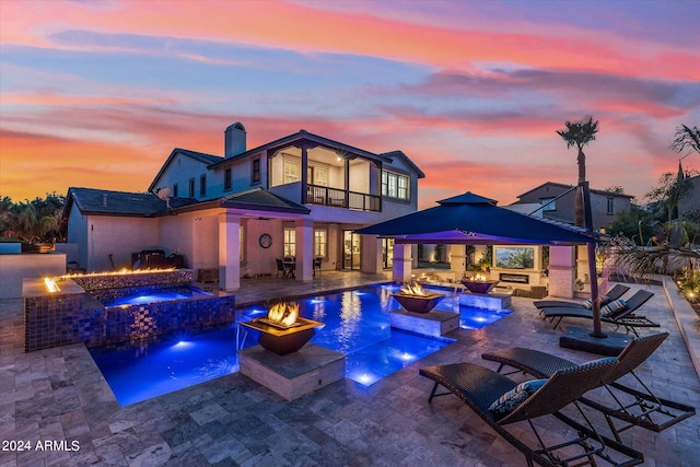 pool at dusk with pool water feature, an outdoor living space with a fire pit, an in ground hot tub, and a patio area