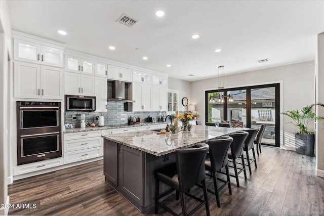 kitchen with appliances with stainless steel finishes, dark wood-type flooring, white cabinetry, and a kitchen island with sink