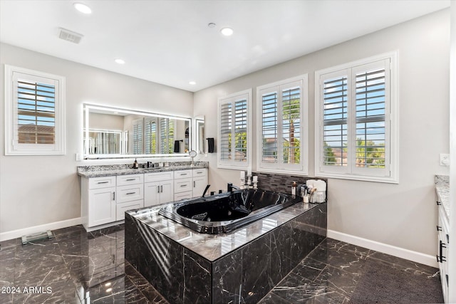 bathroom featuring a relaxing tiled tub, vanity, and a healthy amount of sunlight