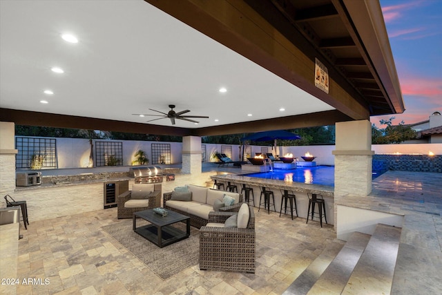 patio terrace at dusk with an outdoor living space, ceiling fan, area for grilling, a grill, and an outdoor bar