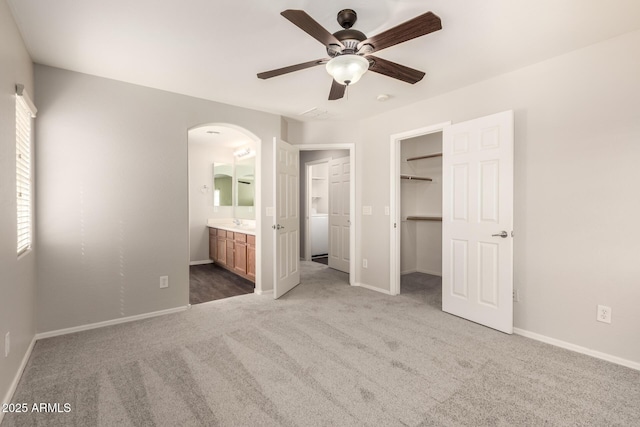 unfurnished bedroom featuring arched walkways, baseboards, a spacious closet, and carpet