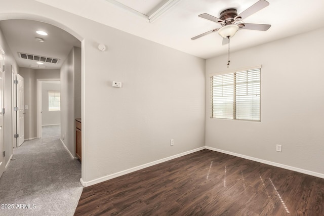 spare room featuring dark wood-style floors, arched walkways, visible vents, a ceiling fan, and baseboards