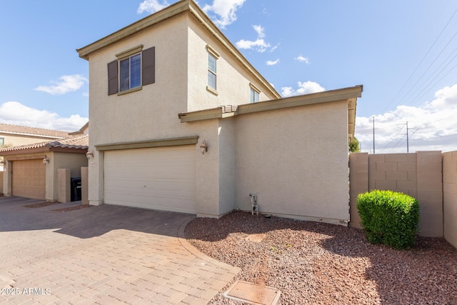 view of property exterior with a garage, fence, decorative driveway, and stucco siding