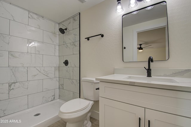 bathroom featuring tiled shower, toilet, ceiling fan, and vanity