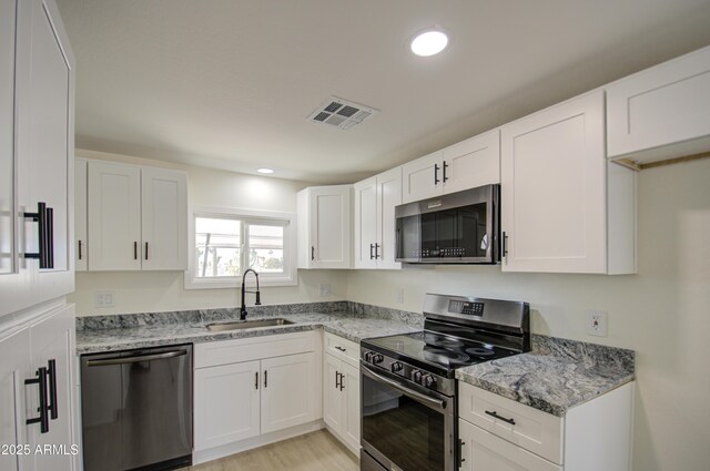 kitchen with light hardwood / wood-style flooring, sink, white cabinets, light stone counters, and stainless steel appliances