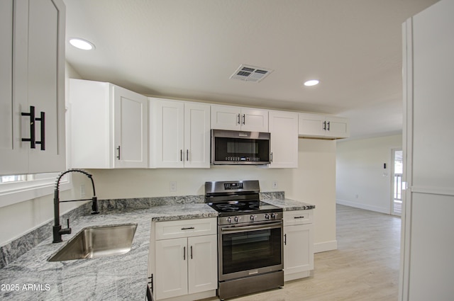 kitchen with a wealth of natural light, appliances with stainless steel finishes, white cabinetry, sink, and light stone counters