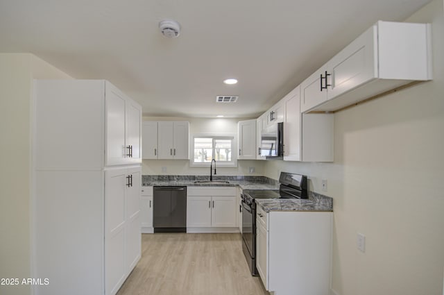 kitchen featuring white cabinets, black appliances, dark stone countertops, sink, and light hardwood / wood-style flooring