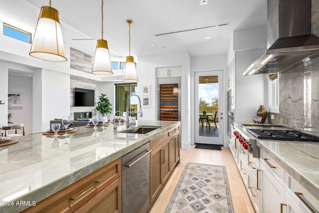 kitchen with white cabinetry, stainless steel appliances, pendant lighting, wall chimney range hood, and sink