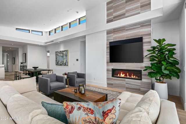 living room featuring a tiled fireplace, light hardwood / wood-style floors, and a towering ceiling