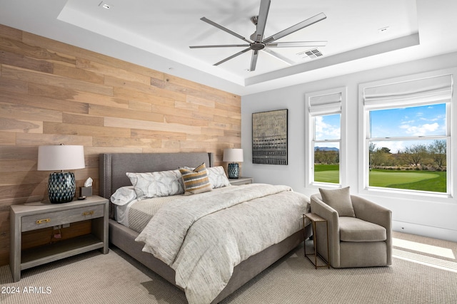 bedroom featuring a raised ceiling, wooden walls, light colored carpet, and ceiling fan