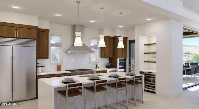 kitchen featuring hanging light fixtures, a breakfast bar area, wine cooler, wall chimney range hood, and stainless steel built in fridge