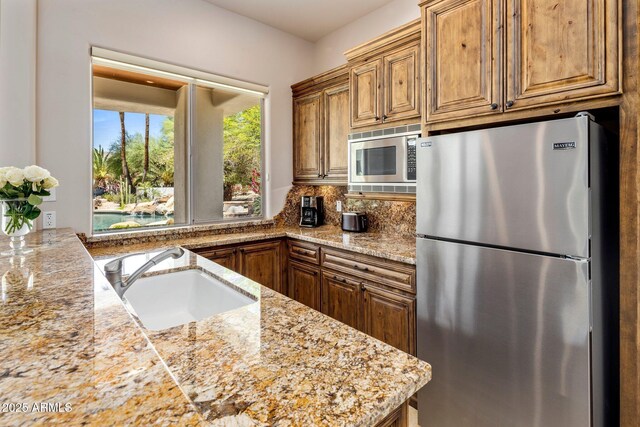 11717 E Estrella Ave, Scottsdale, AZ 85259 - kitchen featuring appliances with stainless steel finishes, a sink, light stone countertops, backsplash, and brown cabinets