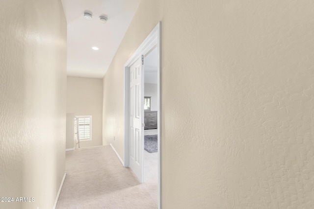 corridor with light colored carpet, baseboards, and a textured wall