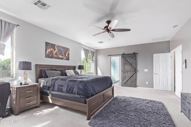 bedroom with a barn door, light colored carpet, visible vents, and a ceiling fan