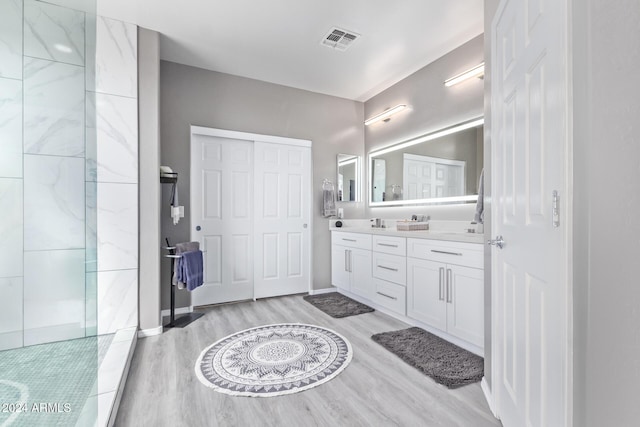 bathroom featuring visible vents, wood finished floors, double vanity, baseboards, and walk in shower