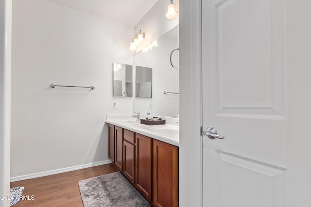 bathroom with double vanity, wood finished floors, baseboards, and a sink