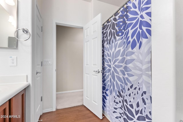 bathroom with a shower with shower curtain, baseboards, wood finished floors, and vanity