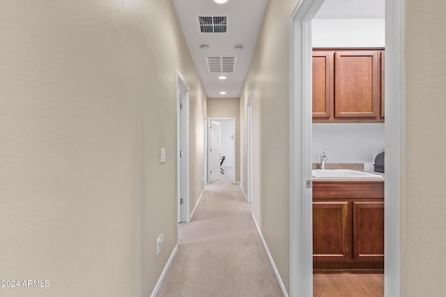 corridor featuring light carpet, visible vents, baseboards, and a sink