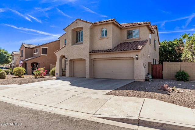 mediterranean / spanish home with fence, a tile roof, stucco siding, driveway, and an attached garage