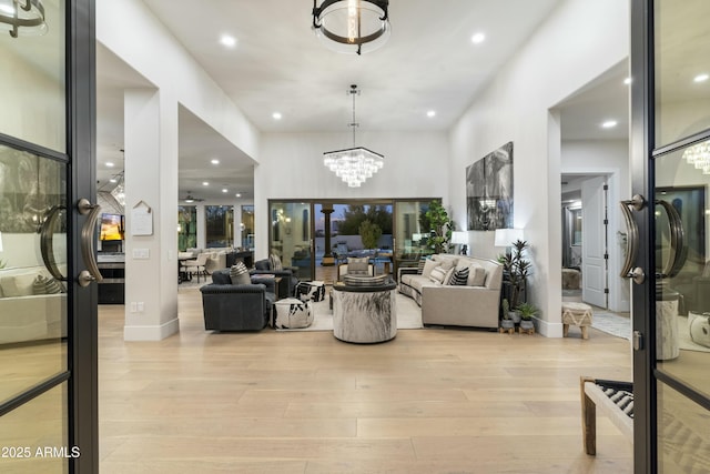 living room with ceiling fan with notable chandelier, light hardwood / wood-style flooring, and french doors