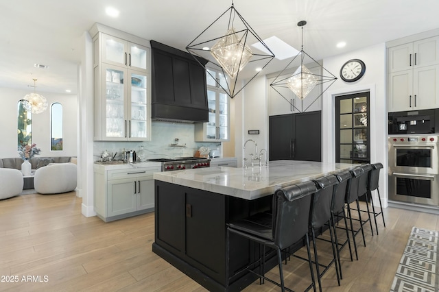 kitchen featuring white cabinetry, a spacious island, hanging light fixtures, light hardwood / wood-style flooring, and light stone counters