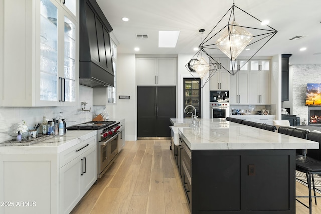 kitchen with decorative light fixtures, a large island with sink, range with two ovens, and white cabinetry