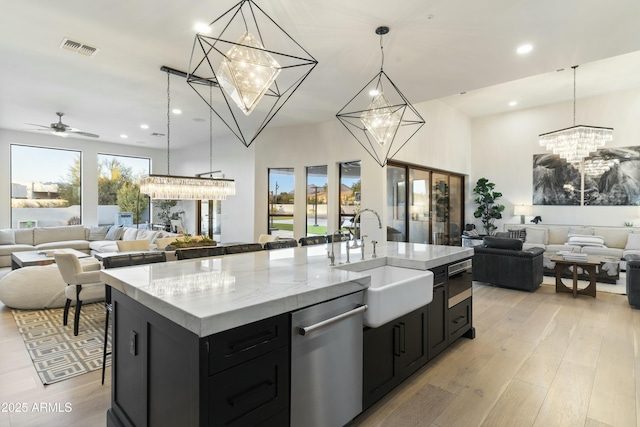 kitchen featuring decorative light fixtures, an island with sink, light hardwood / wood-style floors, sink, and ceiling fan